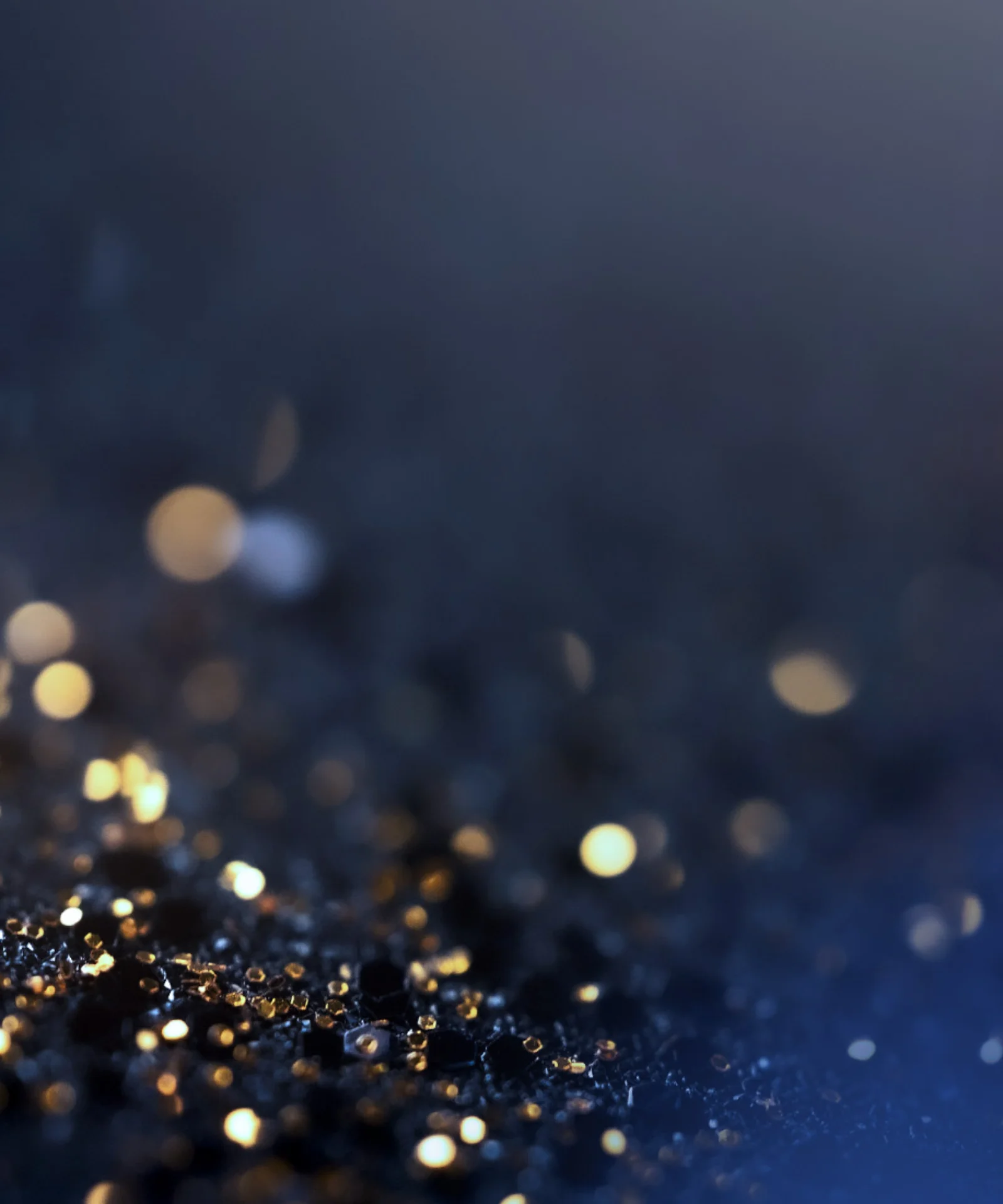 Close-Up of Sparkling Lights on Dark Surface Abstract close-up of golden and blue sparkling lights on a dark surface, with soft bokeh effects in the background.
