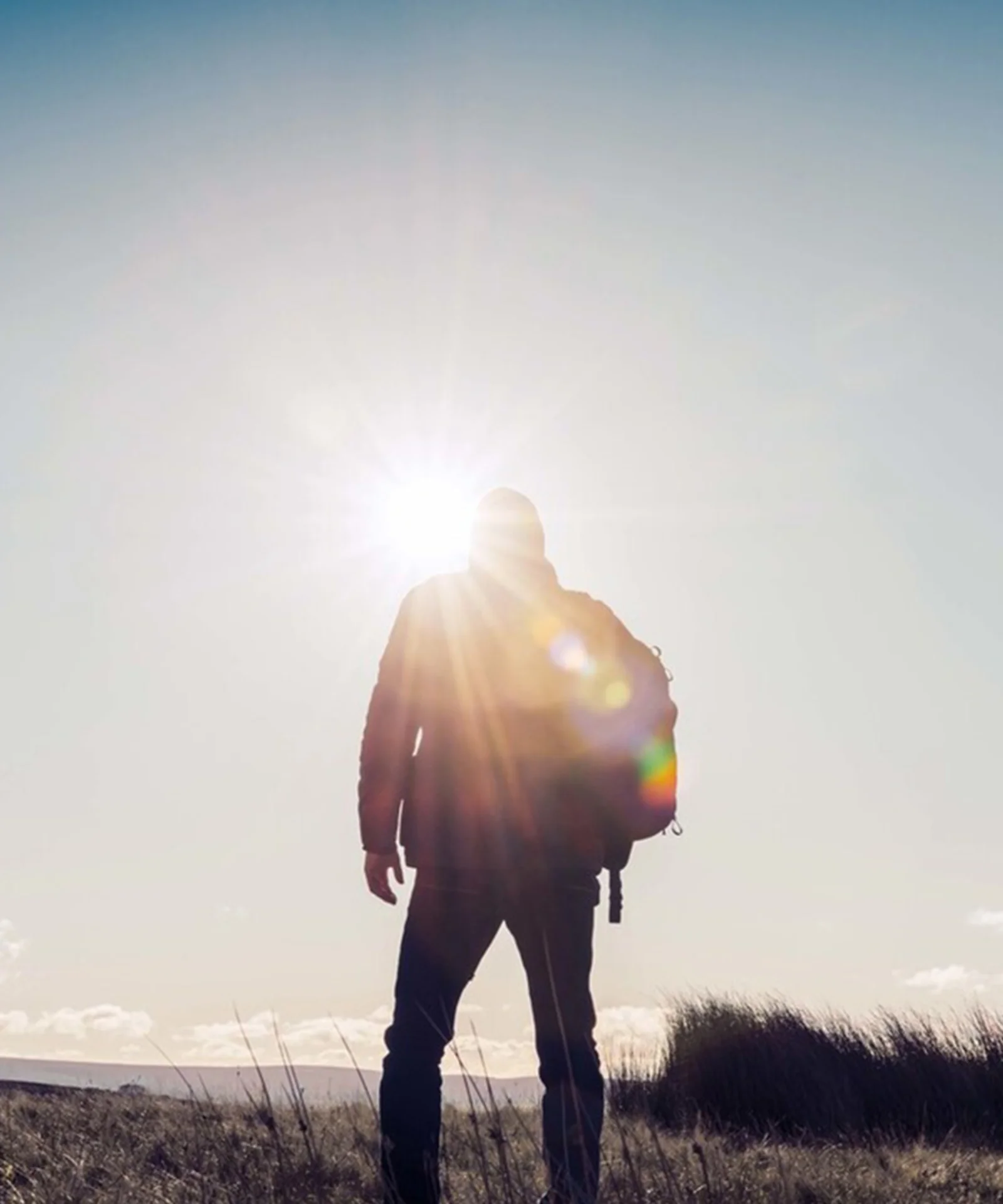 Embracing the Horizon Silhouette of a person standing in a grassy field, with the sun shining brightly in the background.