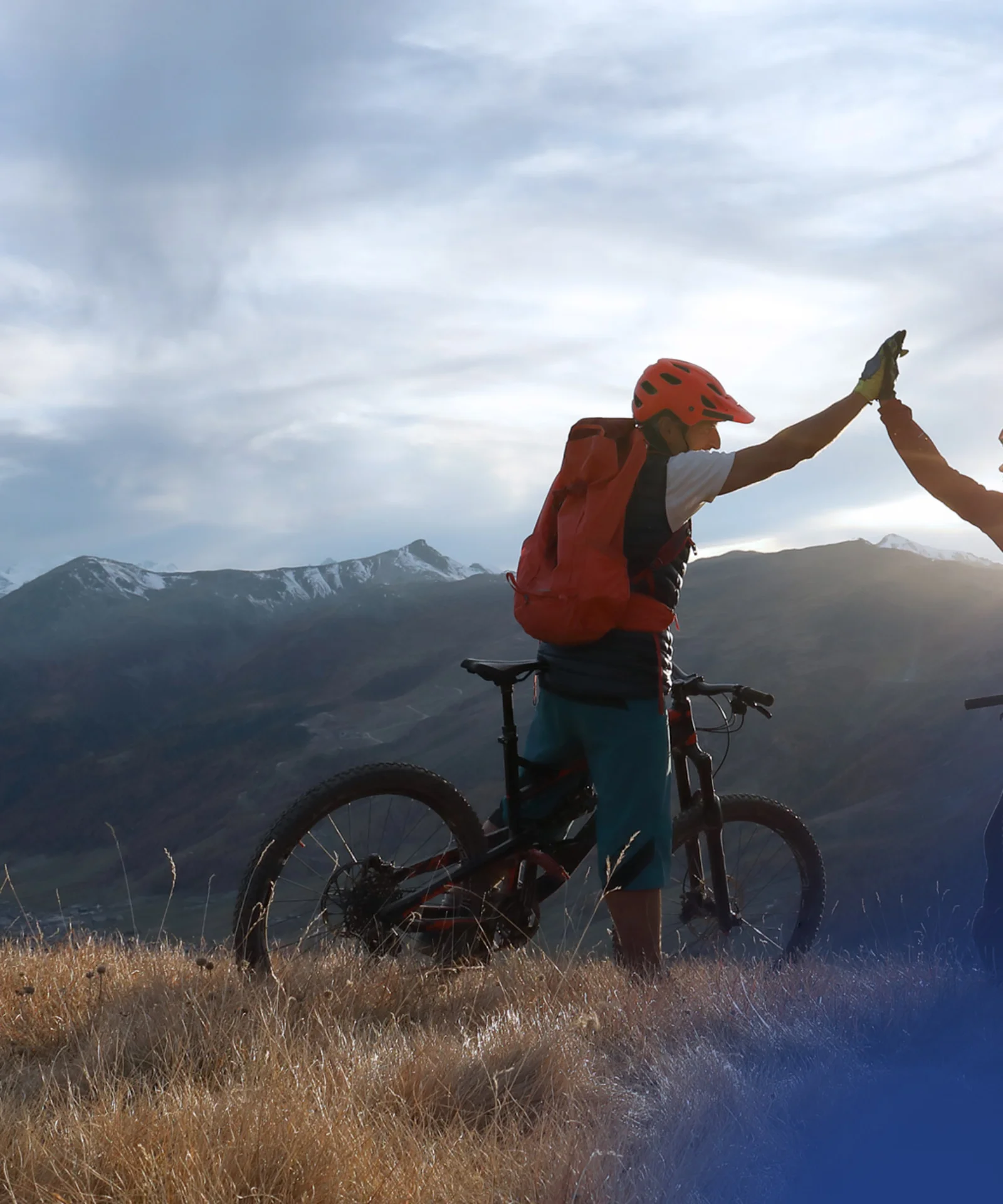 Gemeinsam zum Erfolg: Die Reise der Innovation Zwei Radfahrer geben sich auf einem Berggipfel ein High-Five, im Hintergrund eine atemberaubende Landschaft aus Bergen und Tälern, was Teamwork und gemeinsame Leistung symbolisiert.