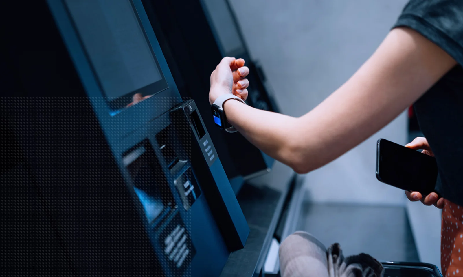 GFT US Blog ICYMI Moneylive 2024 - 3 A person uses a smartwatch to make a contactless payment at a self-service kiosk while holding a smartphone and shopping basket.